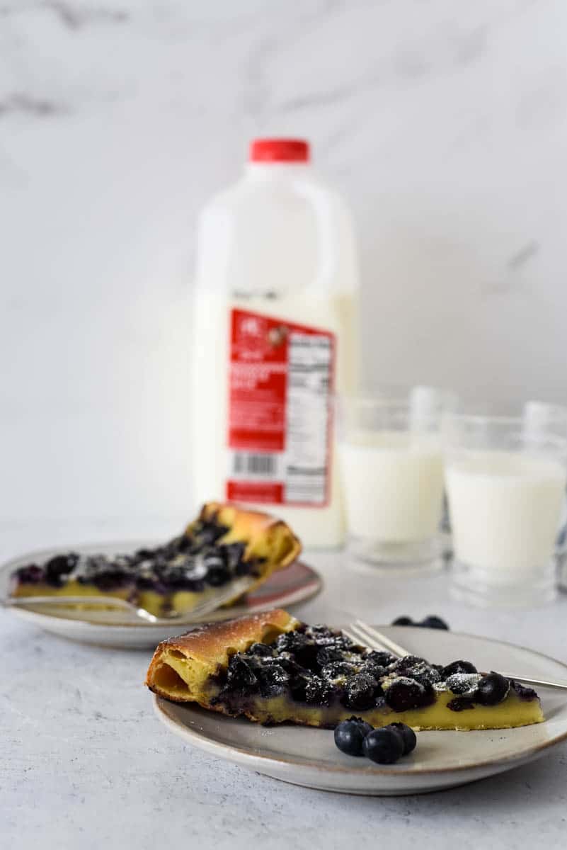 two plates with slices of clafoutis and glasses of milk behind