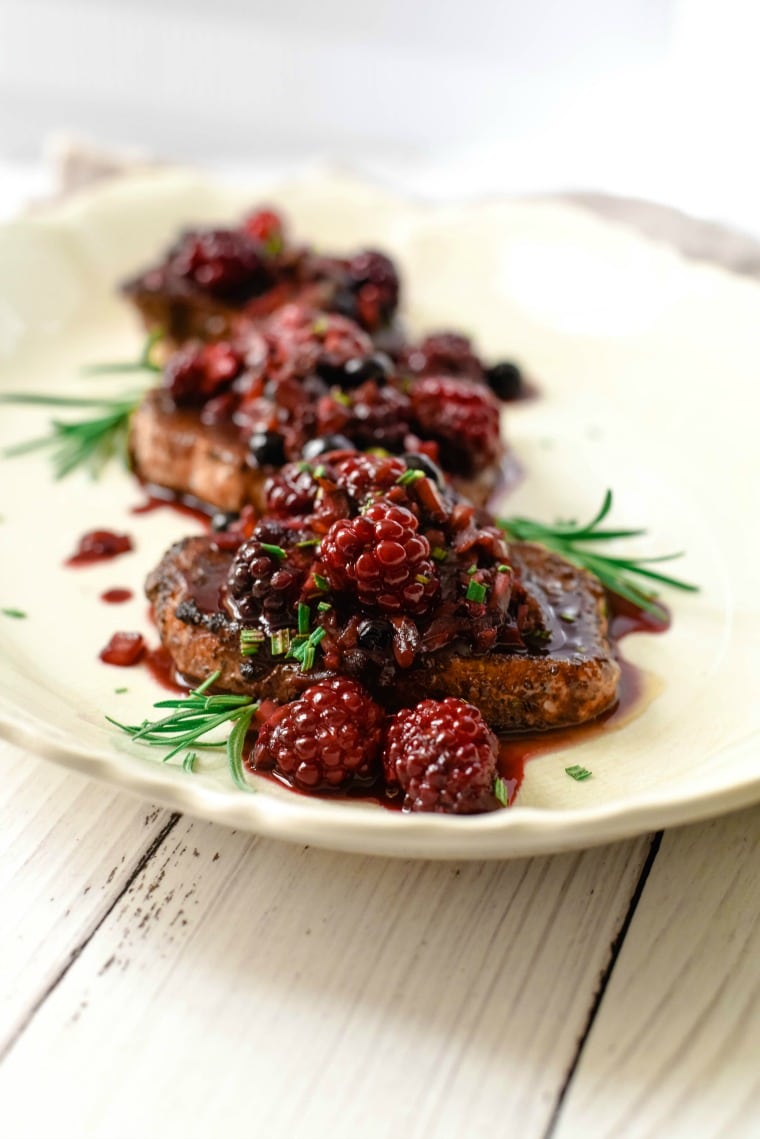 platter of pork chop topped with blackberries and cocoa sauce