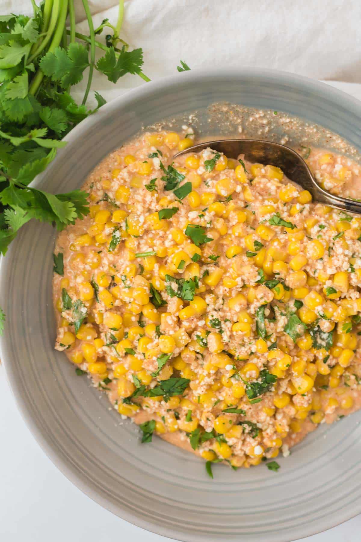 Mexican street corn in grey bowl with serving spoon and cilantro