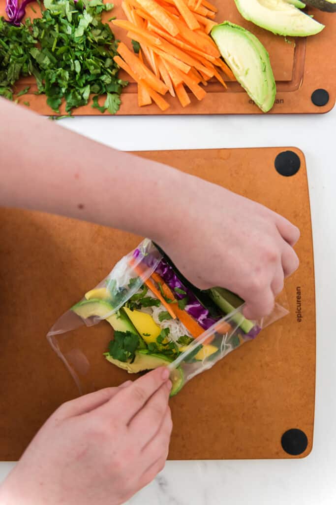 child folding sides of rice wrapper over spring roll fillings