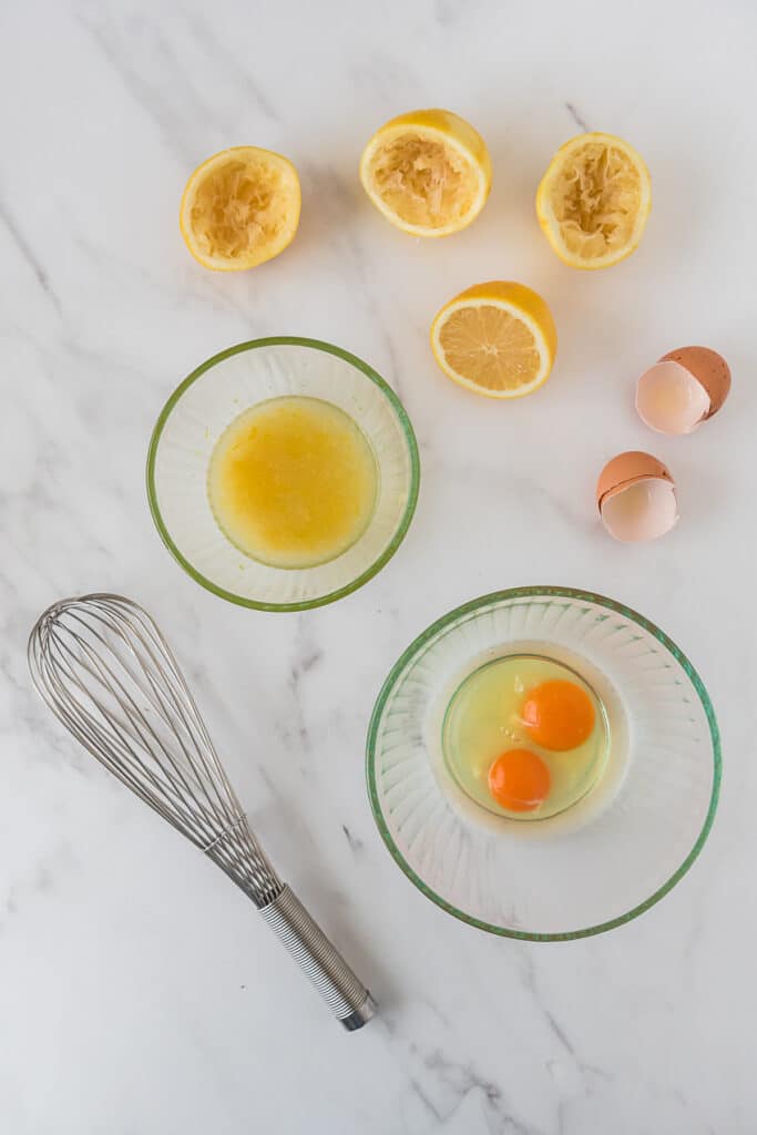 two bowls, one with lemon juice surrounded by lemon peels, and the second with cracked eggs surrounded by egg shells