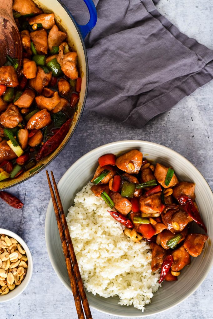 plate of kung poa chicken with rice and chopsticks next to pan