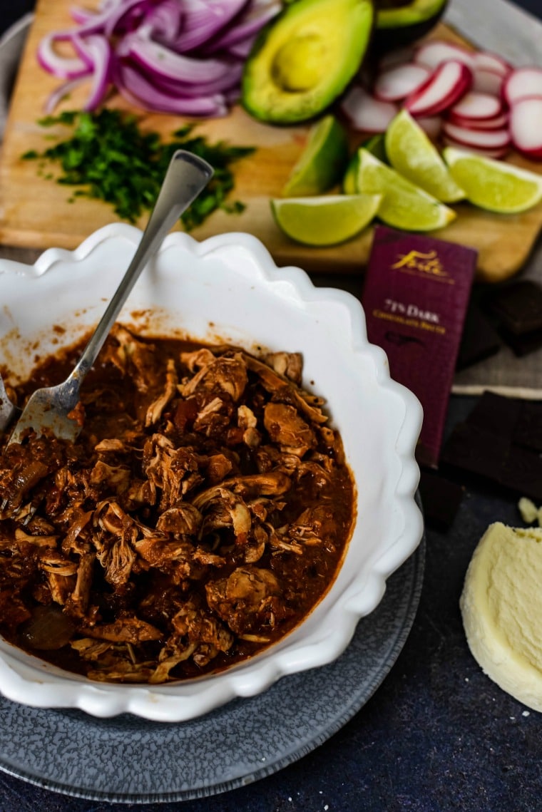 A bowl of Mole and Chicken on a table with limes behind it