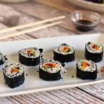 A white rectangular plate with rainbow veggie sushi 