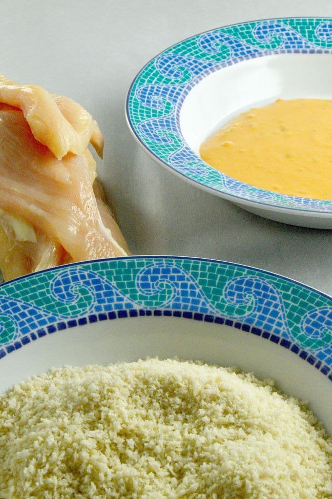 Raw chicken tenders next to two bowl. One bowl with egg wash, and the other bowl with panko bread crumbs.