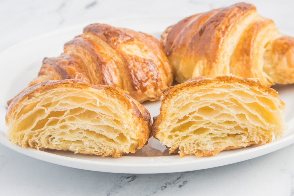 croissant cut in half to show inside layers with more croissants on plate behind