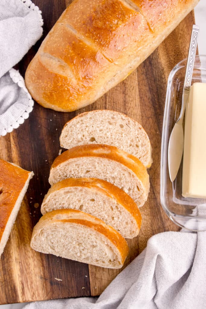 sourdough french bread slices stacked next to second loaf and stick of butter