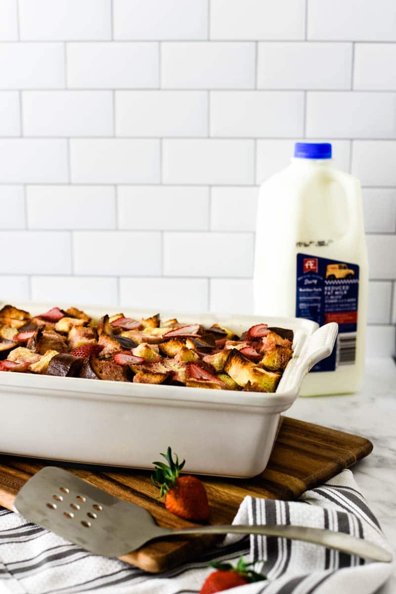 strawberry bread pudding in white stoneware dish with a half gallon of AE 2% milk behind it